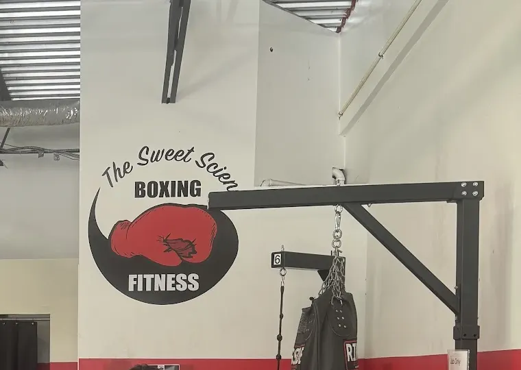 Red glove logo of The Sweet Science Boxing Fitness on a white wall above a red band
