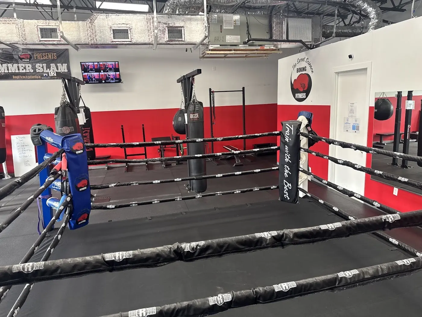 Boxing ring with black ropes, red wall and a corner pad reading Train with the Best at The Sweet Science Boxing Fitness in Cape Coral